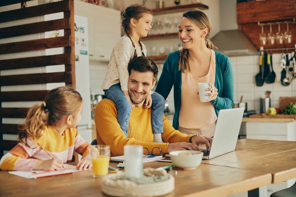 Para na kanapie, mężczyzna siedzi z laptopem na kolanach, kobieta leży z tabletem i opiera głowę na kolanach mężczyzny, oboje się uśmiechają.