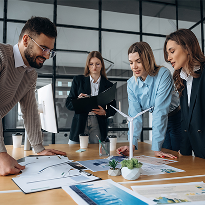 Grupa młodych profesjonalistów w biurze analizująca projekt przy makiecie turbiny wiatrowej.