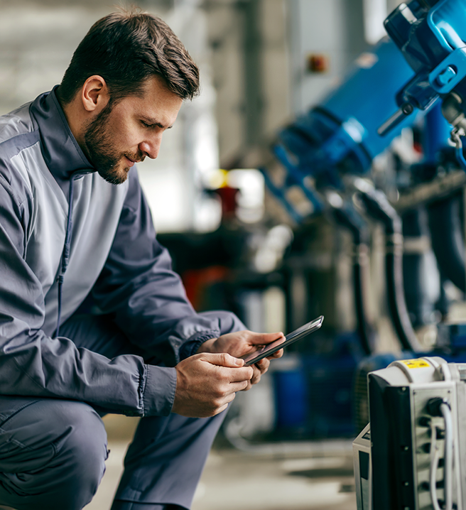Młody mężczyzna obsługuje tablet przed ramieniem robota przemysłowego w hali fabrycznej.