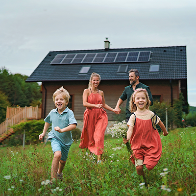 Uśmiechnięta rodzina na tle domu jednorodzinnego z panelami fotowoltaicznymi na dachu.