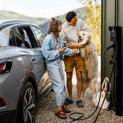 Para młodych ludzi z dużym psem przy samochodzie przed nowoczesnym domem.