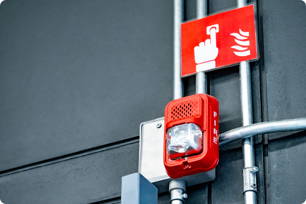 5- Zdjęcie elementów systemu bezpieczeństwa przeciwpożarowego. Urządzenia zamontowane są na jasnej ścianie i stanowią wyposażenie systemu reagowania na sytuacje awaryjne.