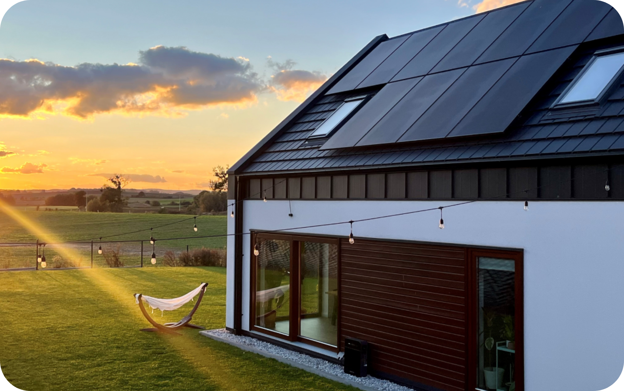 Dom z panelami fotowoltaicznymi na dachu, przy domu magazyn energii marstek Venus, w tle zielone pole.