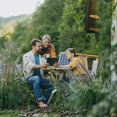 Rodzina siedząca na tarasie, wspólnie przeglądająca tablet w słoneczny dzień.