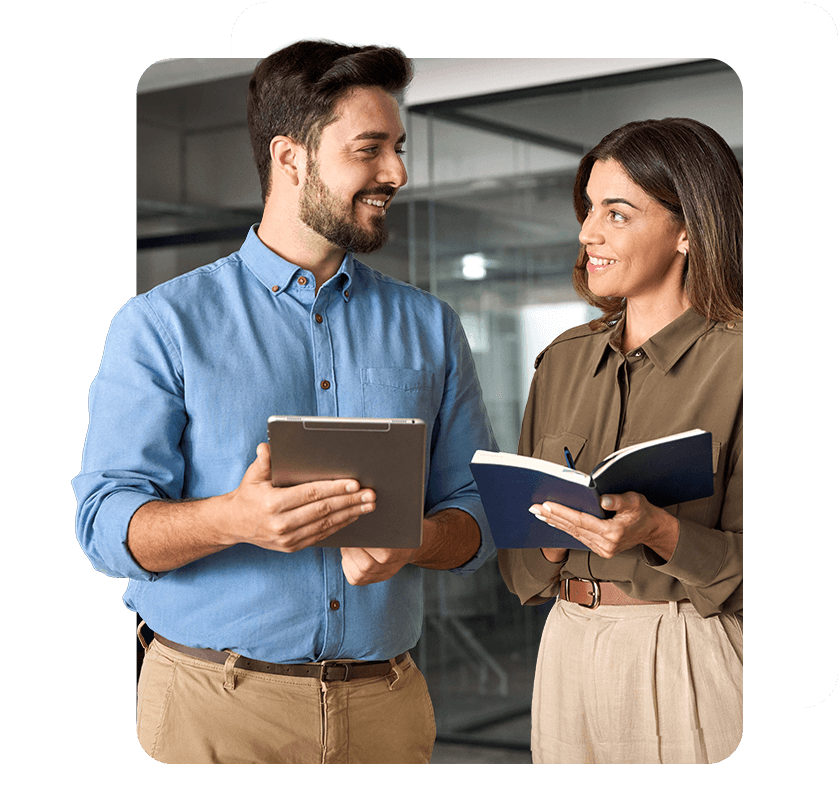 Para biznesowa rozmawia, uśmiechnięta kobieta w eleganckiej koszuli trzyma notes, a mężczyzna tablet.