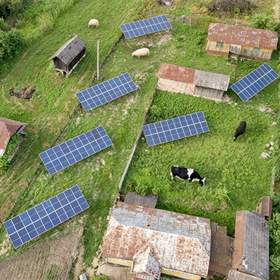 Widok z lotu ptaka na gospodarstwo rolne z panelami słonecznymi ustawionymi na ziemi obok budynków gospodarczych.