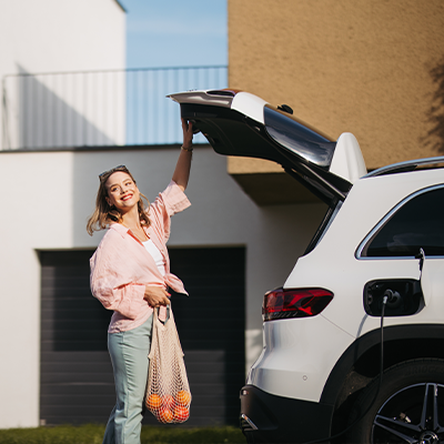 Kobieta chowająca zakupy do bagażnika białego samochodu przed nowoczesnym domem.