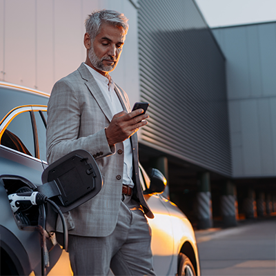 Dojrzały mężczyzna w garniturze korzystający ze smartfona obok nowoczesnego budynku biurowego.